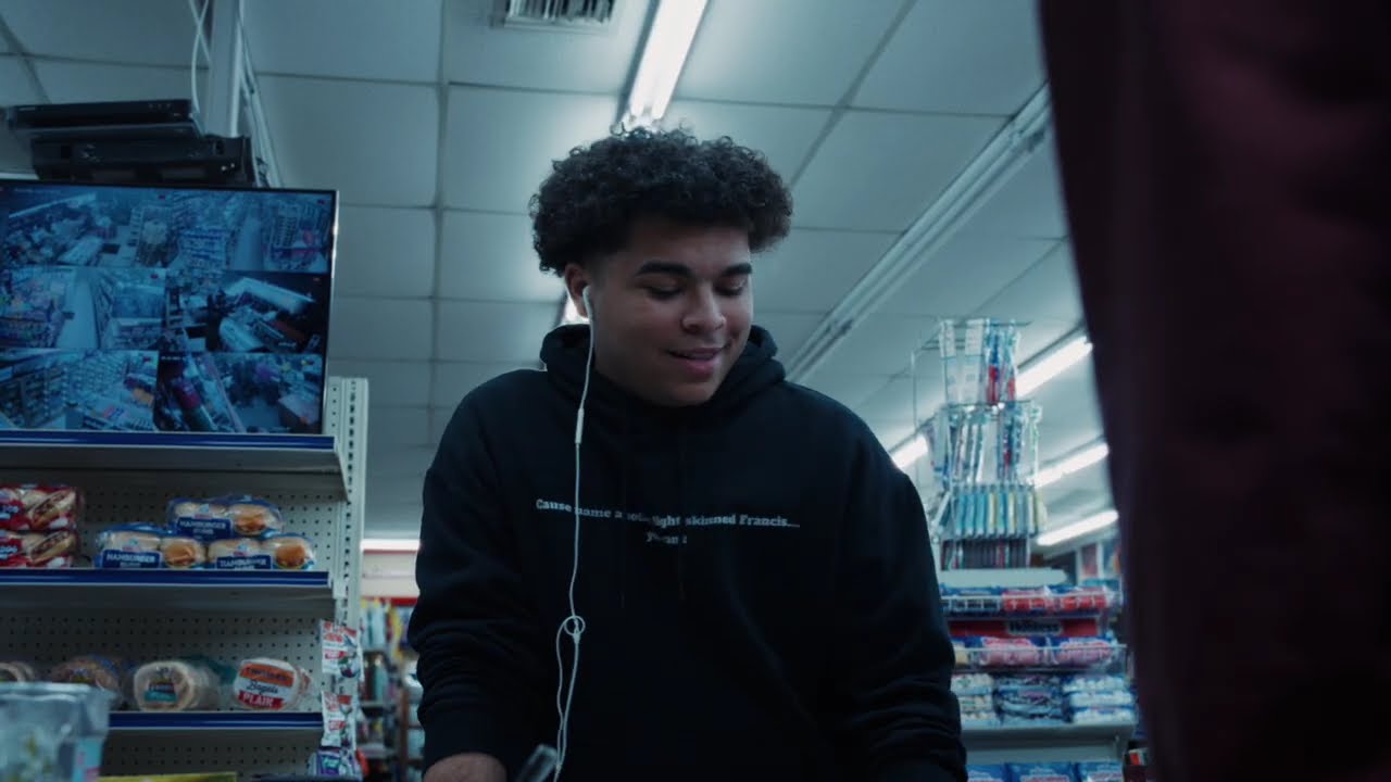 Still from the album teaser — Francis in a black hoodie and earbuds, standing in a corner store